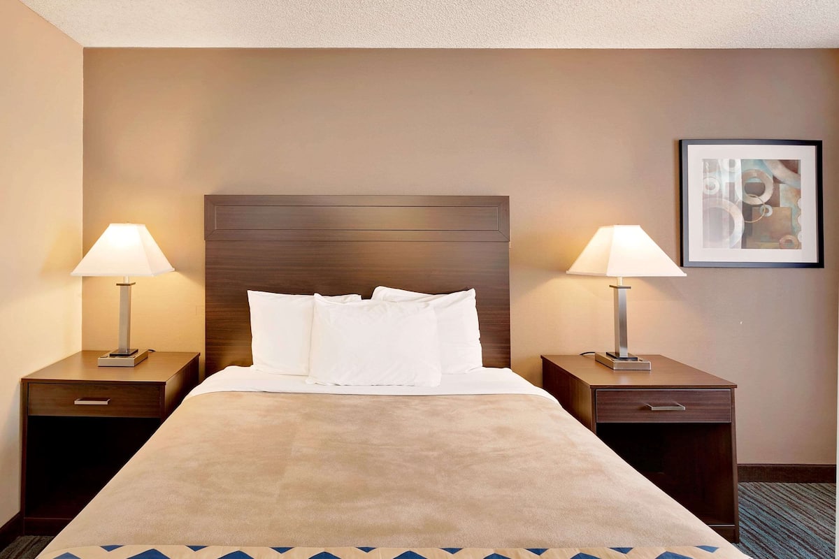 A hotel room with a large bed, two bedside tables with lamps, a headboard, and a framed picture on the wall.