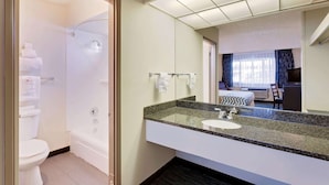 A modern hotel bathroom with a shower, toilet, and a large mirror above the sink.