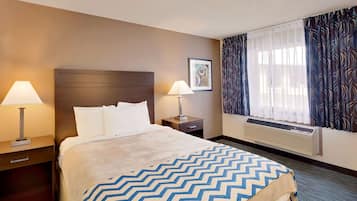 A hotel room with a bed, two bedside tables with lamps, a window with curtains, and a wall-mounted air conditioner.