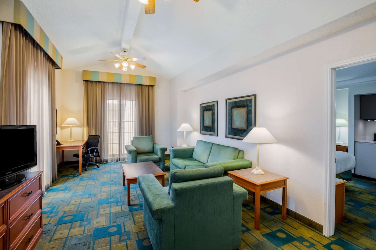 A hotel room with a TV, green sofas, a desk, and a ceiling fan.