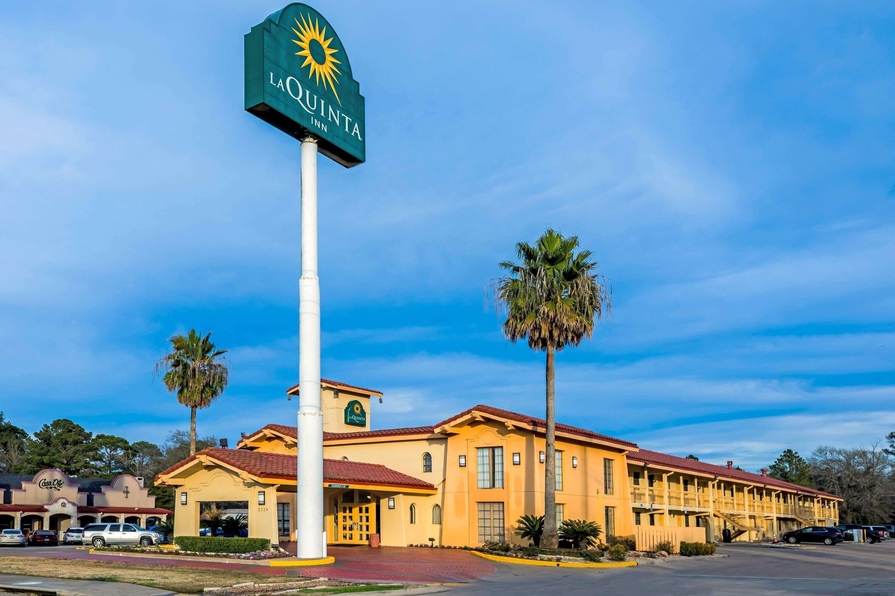 Un La Quinta Inn con un letrero grande, techo de tejas rojas y palmeras.