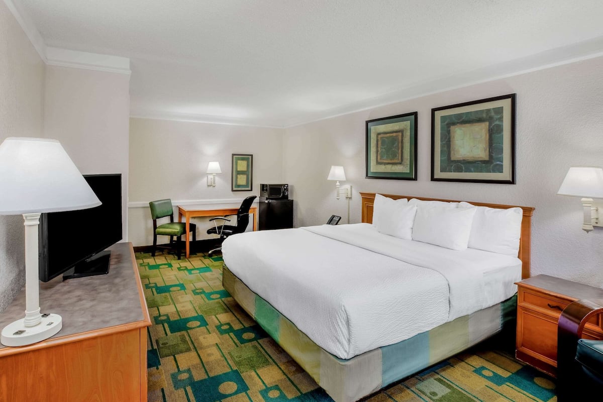A hotel room with a bed, desk, chair, TV, and lamps.