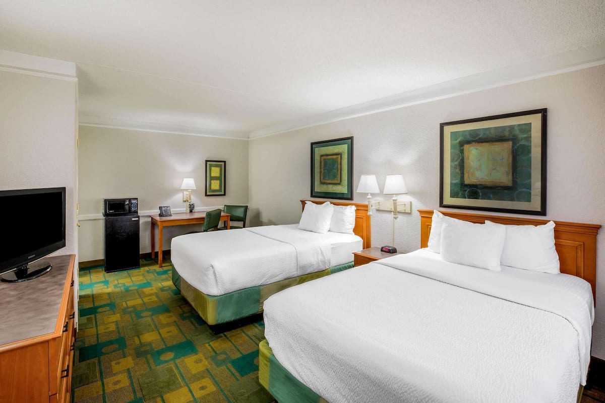 A hotel room with two beds, a television, a desk with a lamp, and artwork on the walls.