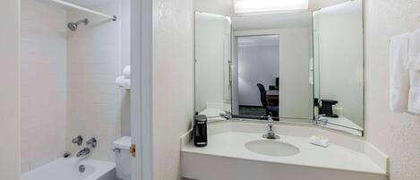 A modern bathroom with a white bathtub, a toilet, a sink with a mirror above it, and a showerhead.