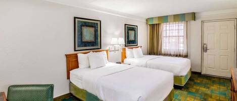A hotel room with two beds, a chair, a desk, and a door.