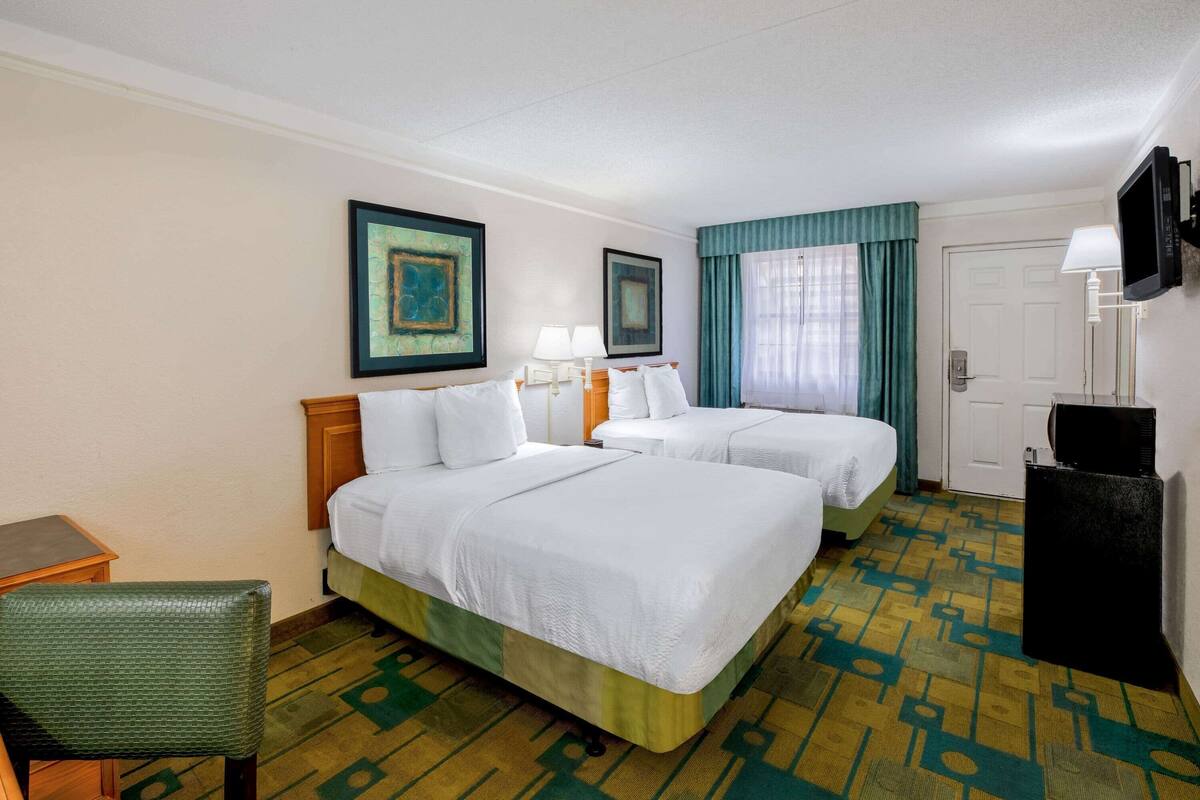 A hotel room with two beds, a desk, a chair, a television, and a door.