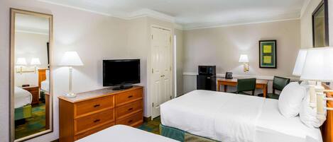 Habitación de hotel con dos camas, televisión, escritorio con silla, espejo y lámpara.