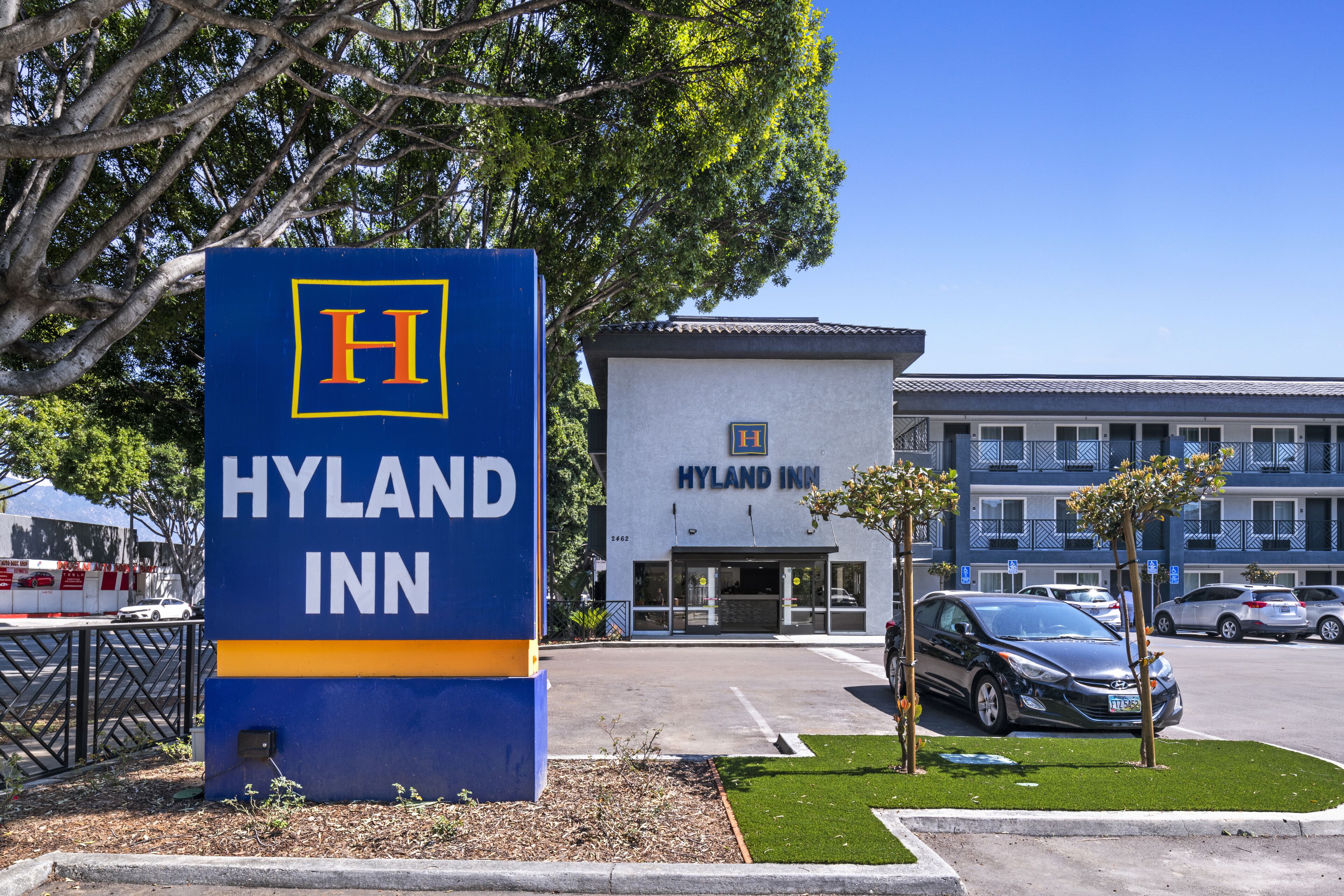 Une enseigne et un bâtiment de l’hôtel Hyland Inn, avec un parking et des voitures.