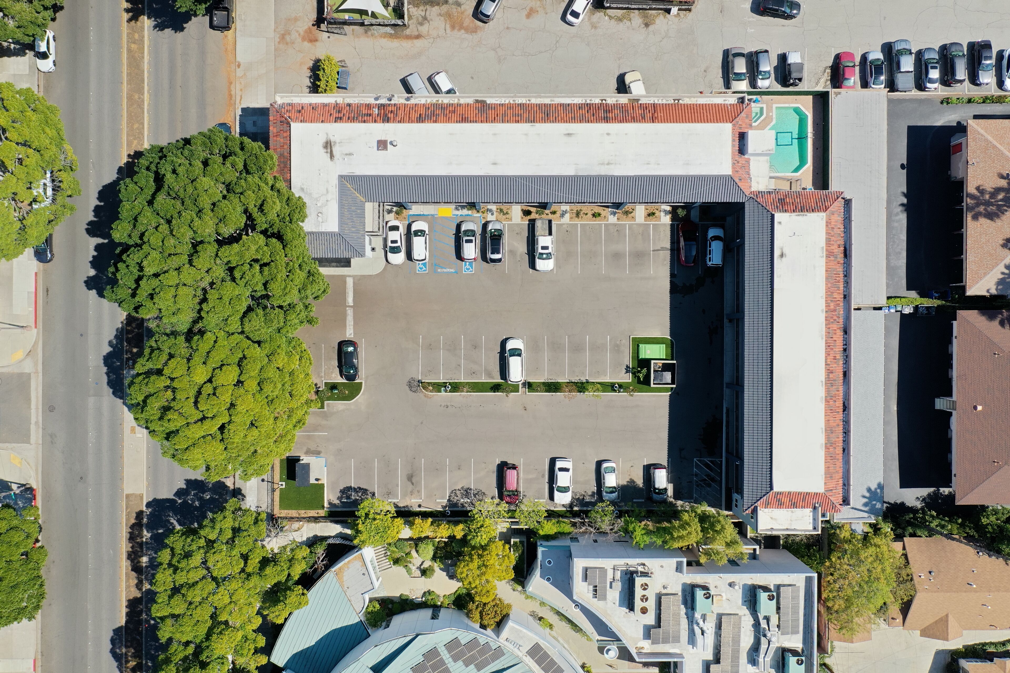 Vista aerea di un parcheggio con diverse auto, un albero grande e un edificio con tetto rosso.