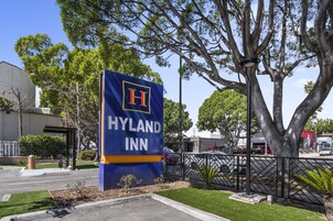 Un letrero de HYLAND INN con un gran logotipo en forma de 'H', rodeado de árboles y un estacionamiento.