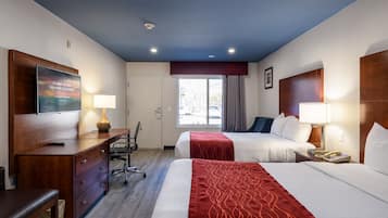 A hotel room with two beds, a desk, a chair, a TV, and a window with curtains.