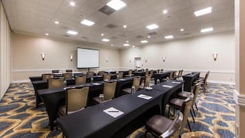 A conference room with multiple tables, chairs, a projector screen, and a carpeted floor.