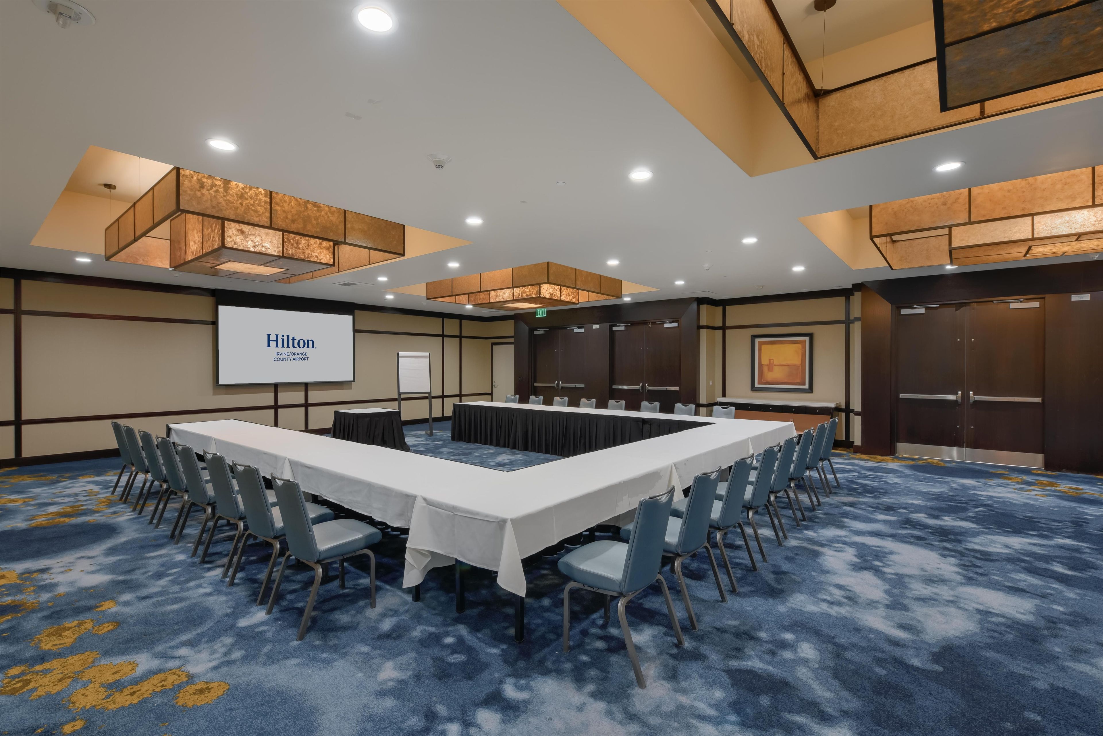 A conference room with a long table, chairs, a projector screen, and a carpeted floor.