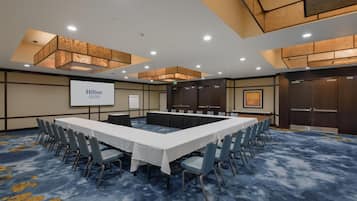 A conference room with a long table, chairs, a projector screen, and a carpeted floor.