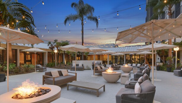 An outdoor seating area with fire pits, umbrellas, and lounge chairs. - Hilton Irvine/Orange County Airport (Irvine)