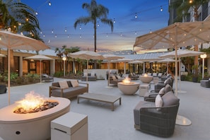 An outdoor seating area with fire pits, umbrellas, and lounge chairs. - Hilton Irvine/Orange County Airport (Irvine)