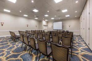 A conference room with rows of chairs, a projector screen, and a carpeted floor.