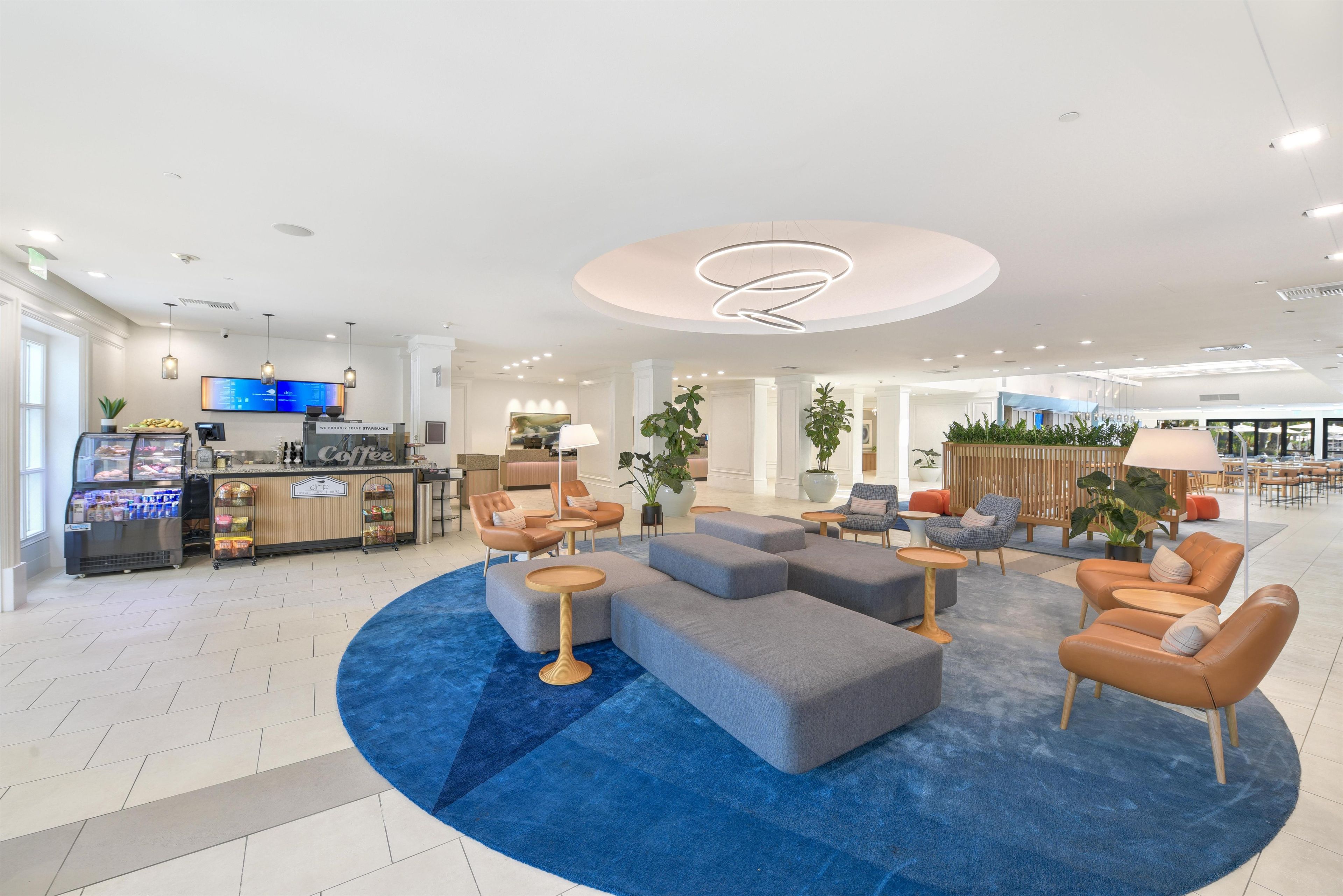 Un moderno vestíbulo de hotel con una zona de estar central, una estación de café y una mesa de recepción.