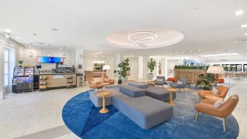 Un moderno vestíbulo de hotel con una zona de estar central, una estación de café y una mesa de recepción.