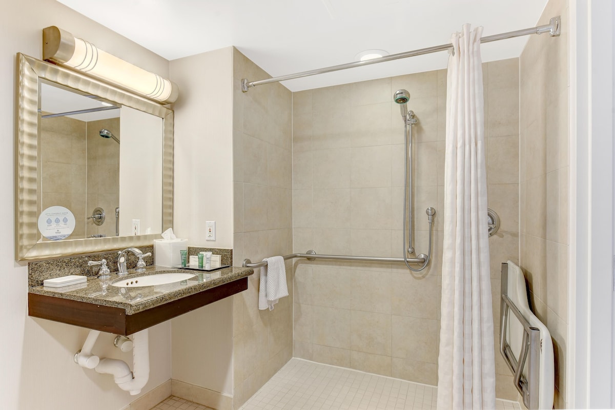 Un baño con lavamanos, espejo, ducha y barras de apoyo.