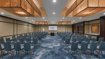 A conference room with rows of chairs, a podium, and a Hilton logo on the screen.