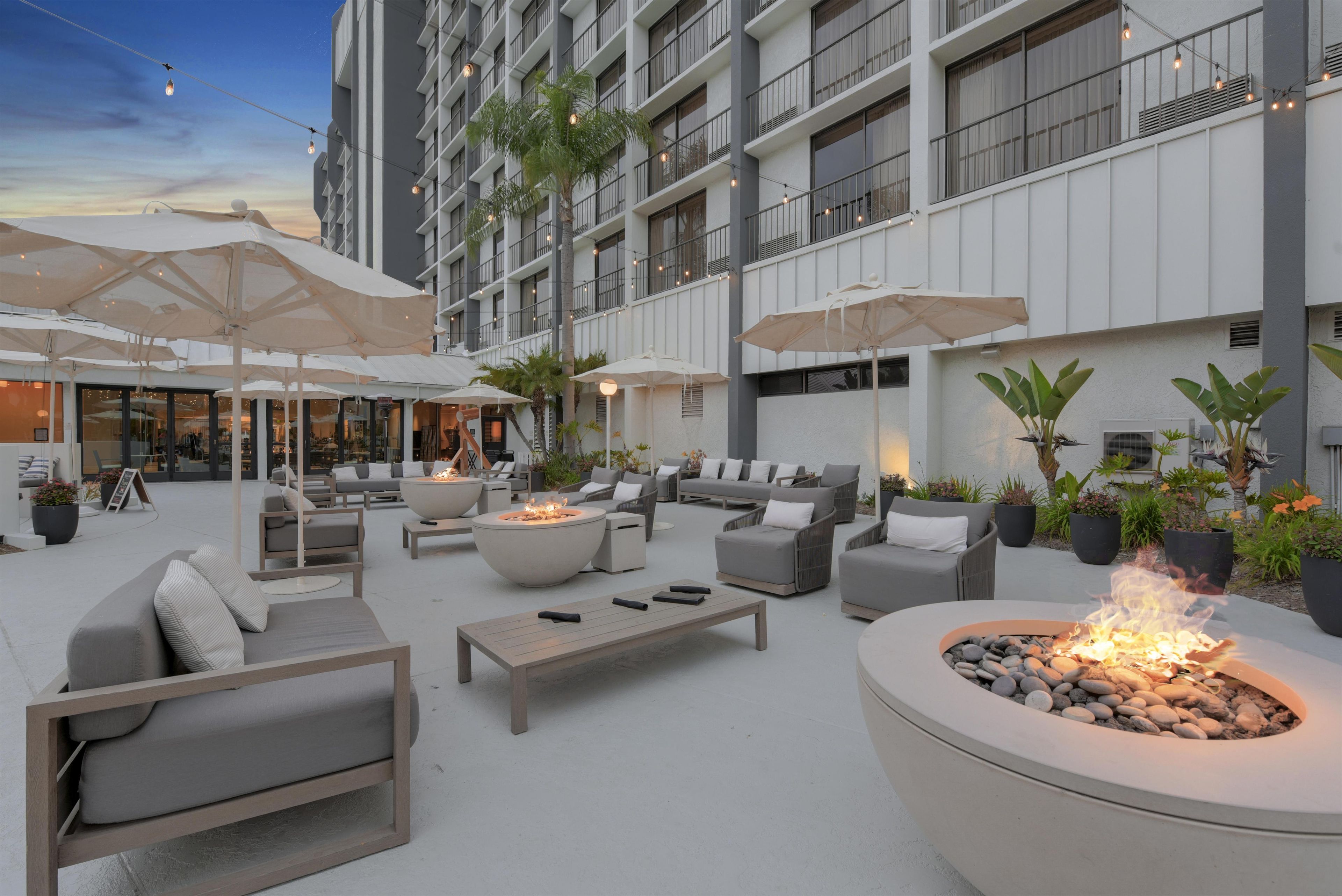 A modern outdoor lounge area with seating, fire pits, and umbrellas.