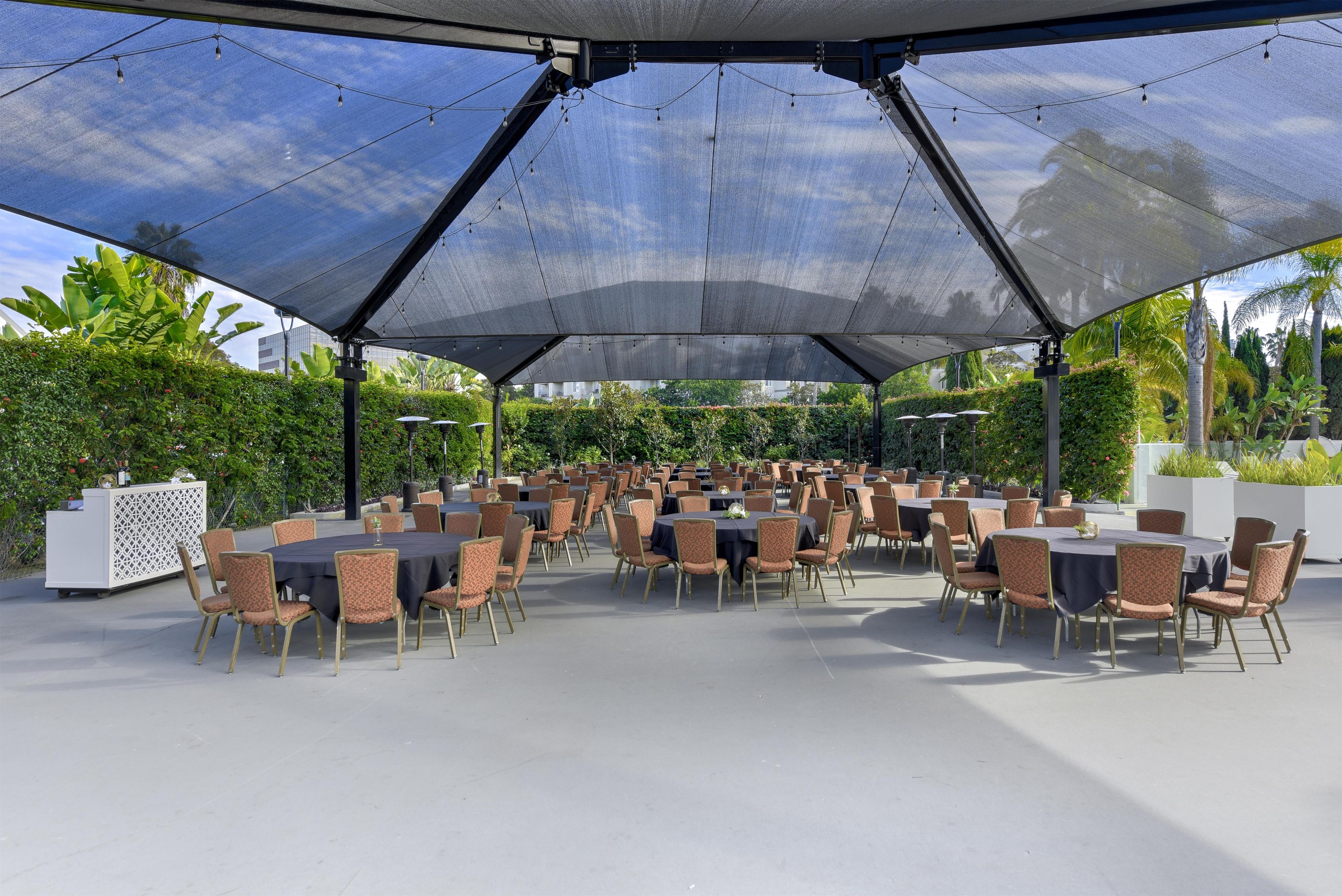An outdoor dining area with round tables and chairs, covered by a large canopy.