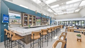 A modern bar area with a long counter, bar stools, and a seating area with tables and chairs. - Hilton Irvine/Orange County Airport (Irvine)