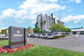 A Hilton hotel with a parking lot, a sign, and a building with multiple floors and a modern design. - Hilton Irvine/Orange County Airport (Irvine)