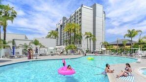 A swimming pool area with lounge chairs, palm trees, and a building in the background. - Hilton Irvine/Orange County Airport (Irvine)