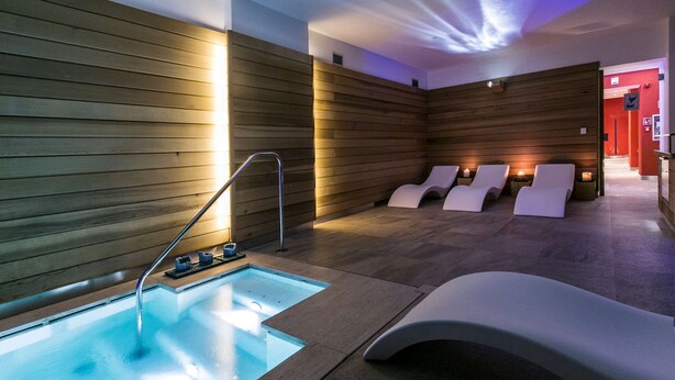 A modern spa with a heated pool, wooden walls, and lounge chairs.