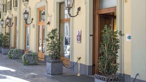 A hotel entrance with a sign reading "Hotel Genova," featuring a classic architectural style with arched windows and potted plants.