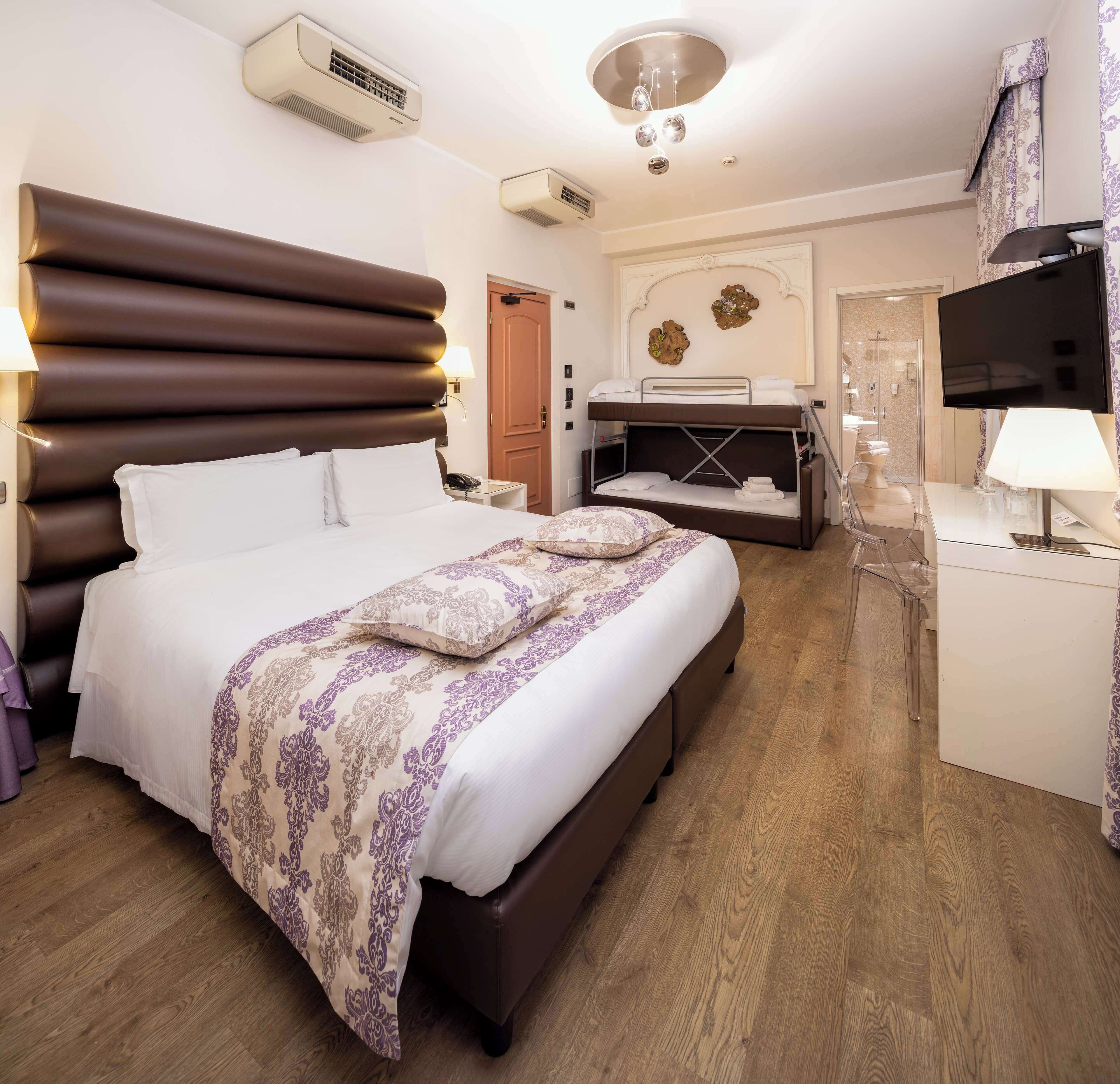 Camera d'albergo con un letto grande, un letto più piccolo a terra, una scrivania con una sedia, una televisione e un bagno visibile attraverso una porta aperta.