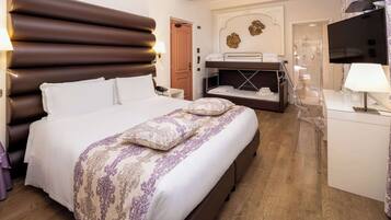 Camera d'albergo con un letto grande, un letto più piccolo a terra, una scrivania con una sedia, una televisione e un bagno visibile attraverso una porta aperta.