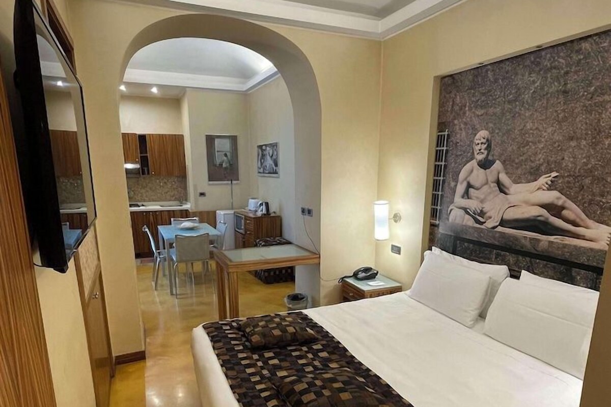 A hotel room with a large bed, a desk, and a chair in the background.