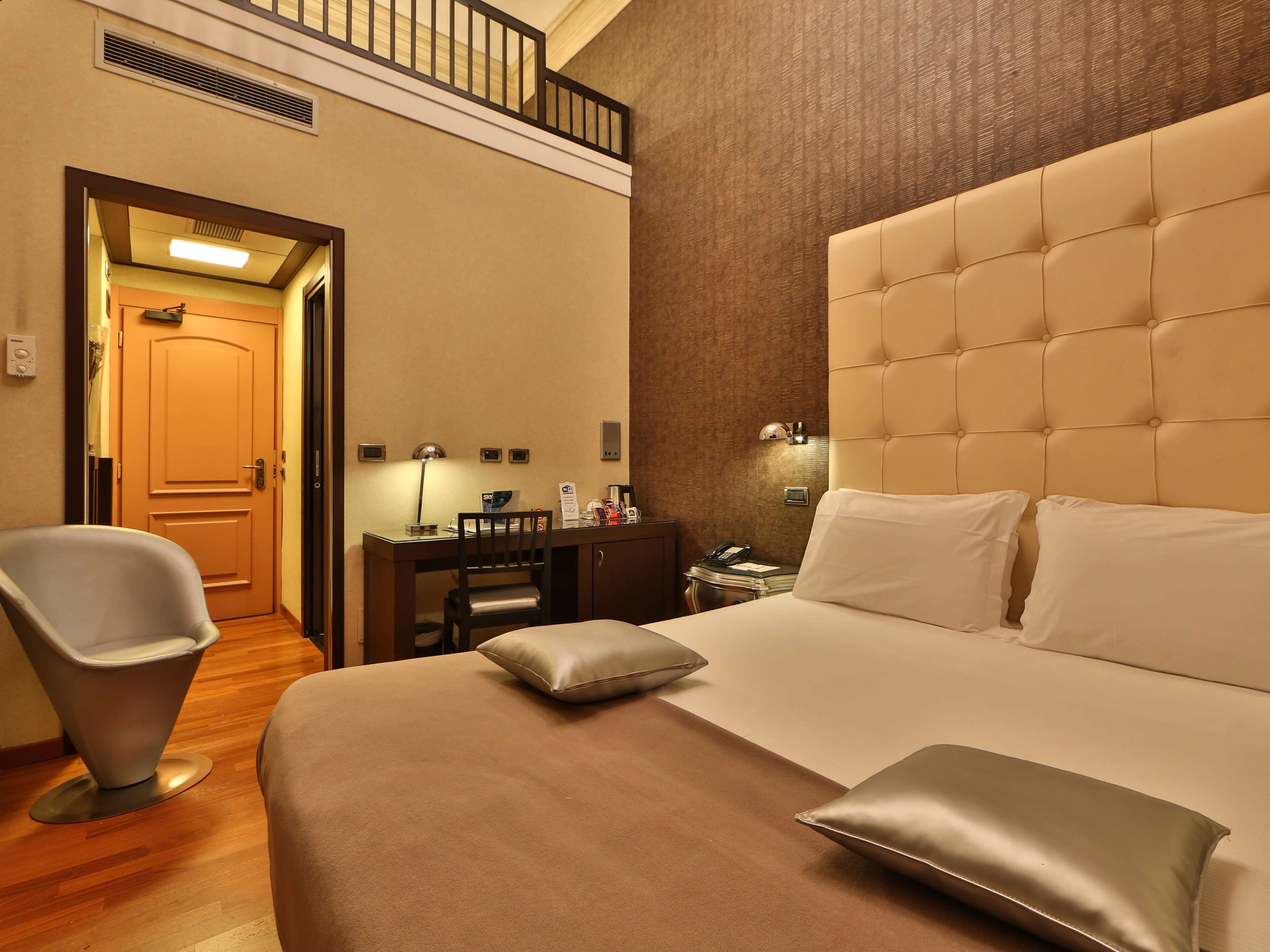 Ein Hotelzimmer mit einem großen Bett, einem Schreibtisch mit Stuhl, einem Telefon und einem Nachttisch.