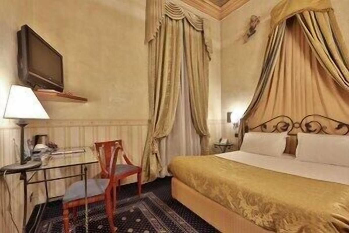 A hotel room with a bed, a chair, a desk, a lamp, curtains, and a television.