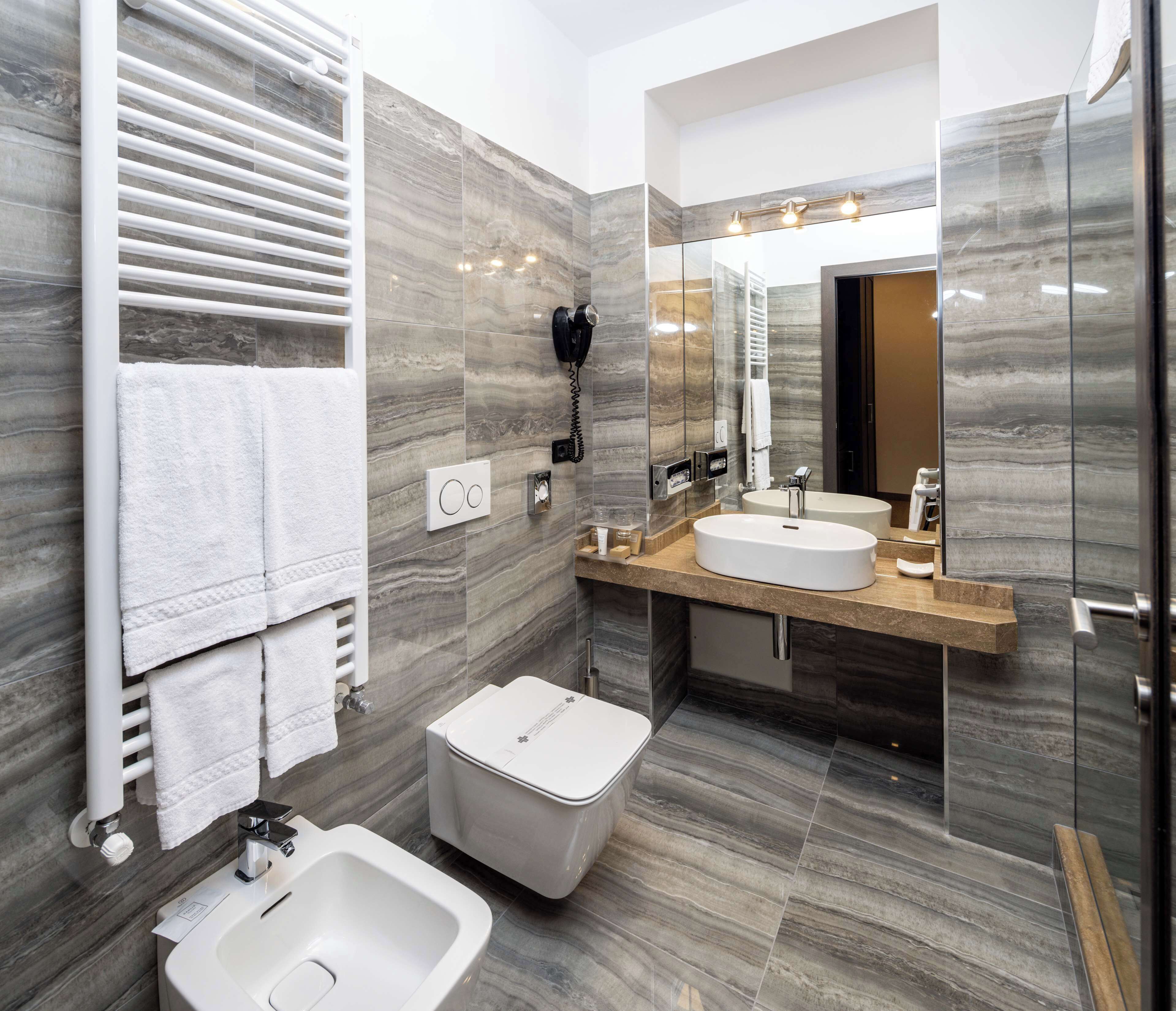 Un baño moderno con un bidé, inodoro, lavamanos y un espejo grande.