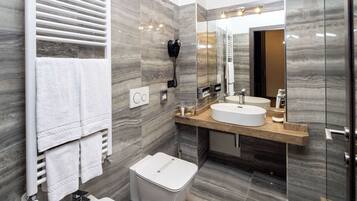 Un baño moderno con un bidé, inodoro, lavamanos y un espejo grande.