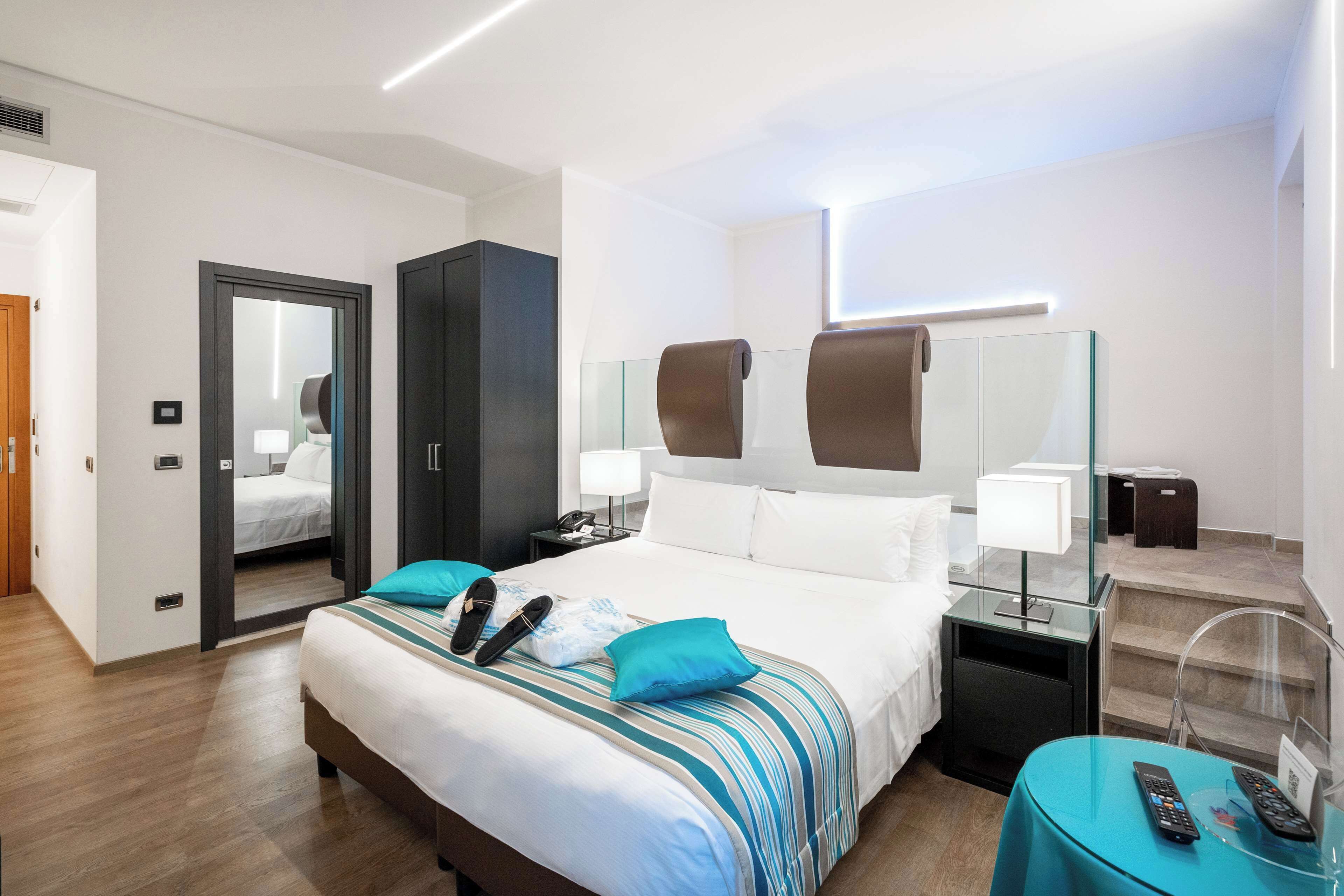 A modern hotel room with a large bed, a desk, a chair, a mirror, and a small table with a remote control.