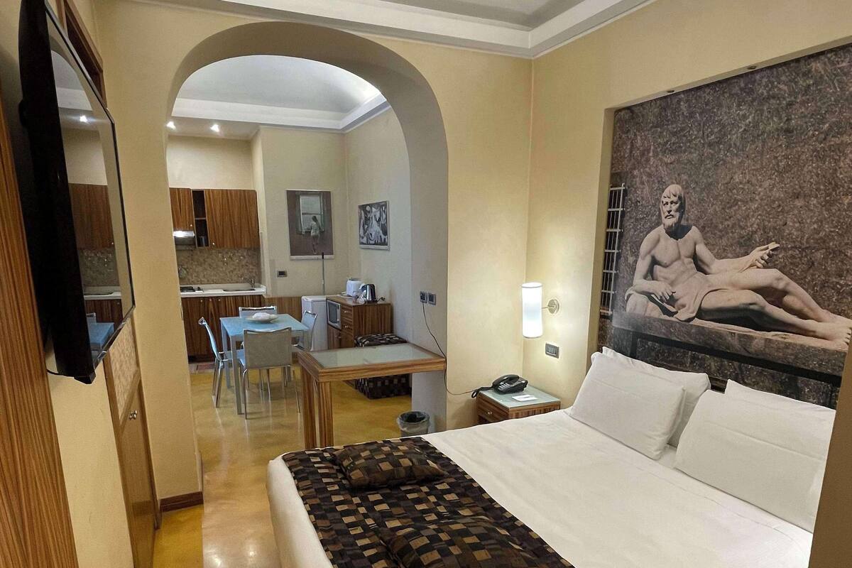 A hotel room with a large bed, a desk, a chair, a television, and a painting on the wall.