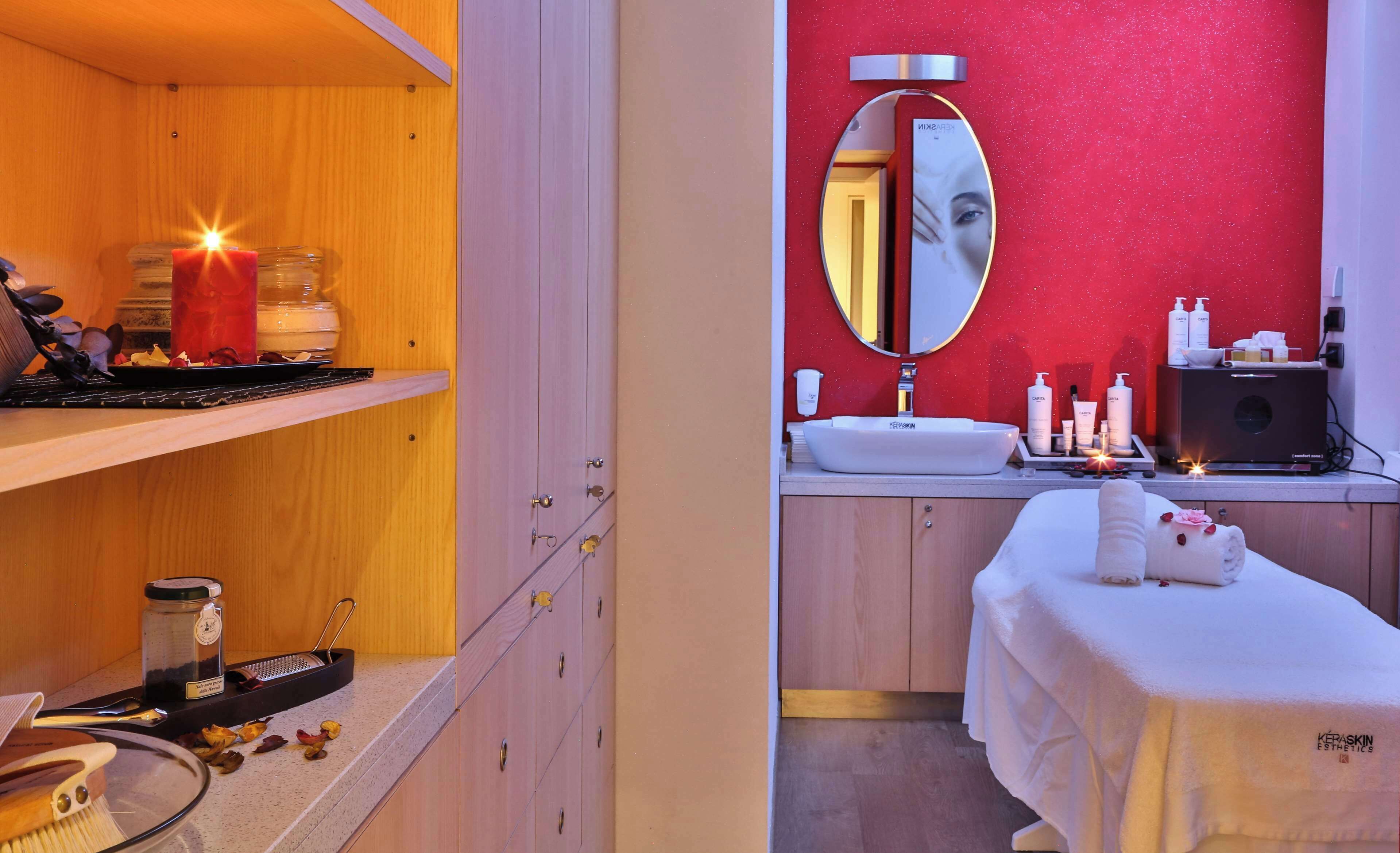 Une salle de spa avec une étagère en bois, une bougie, un pot et une table de massage recouverte de serviettes.