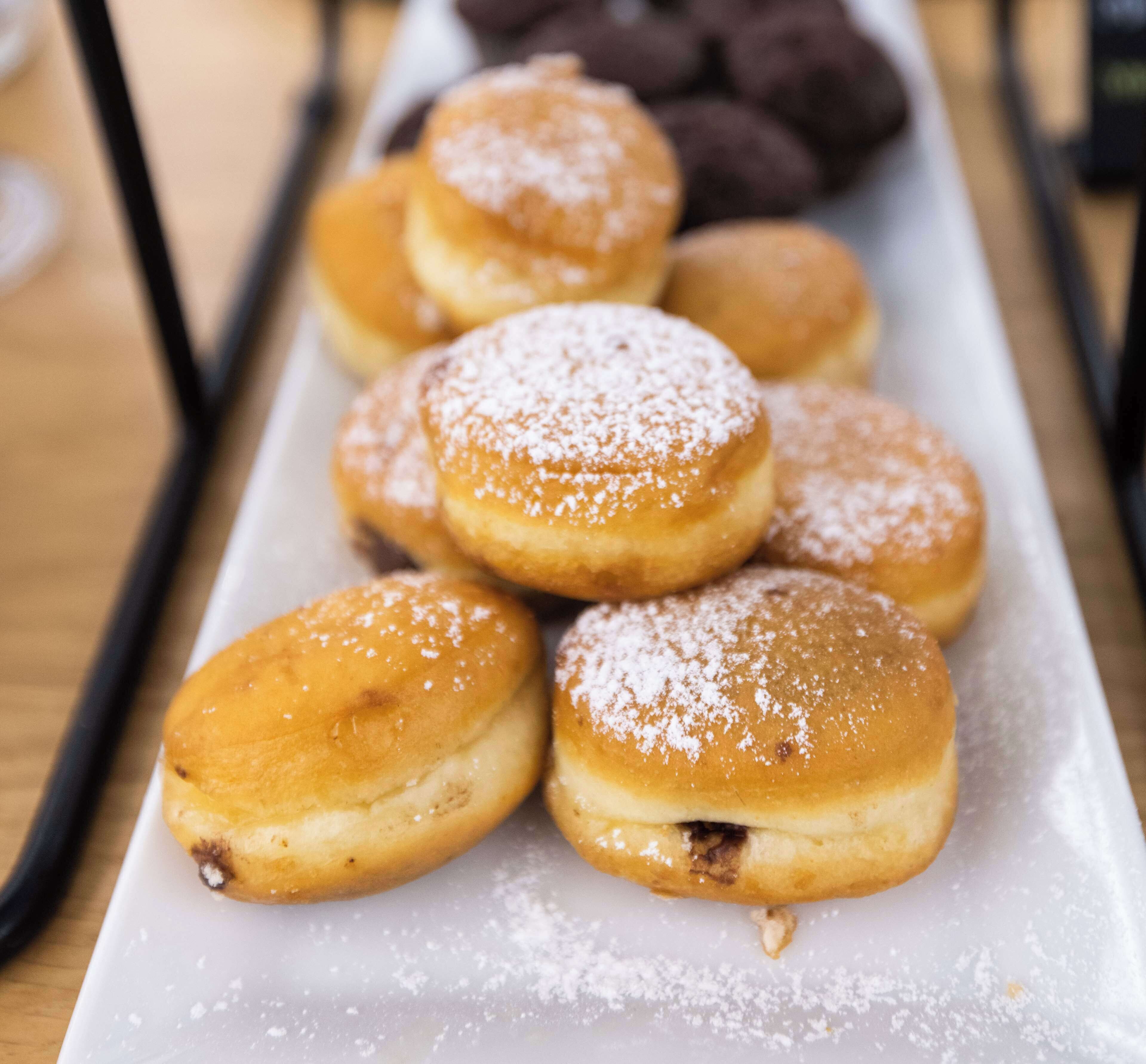 Un vassoio con dolci ricoperti di zucchero a velo, forse delle ciambelle, su un piatto bianco.