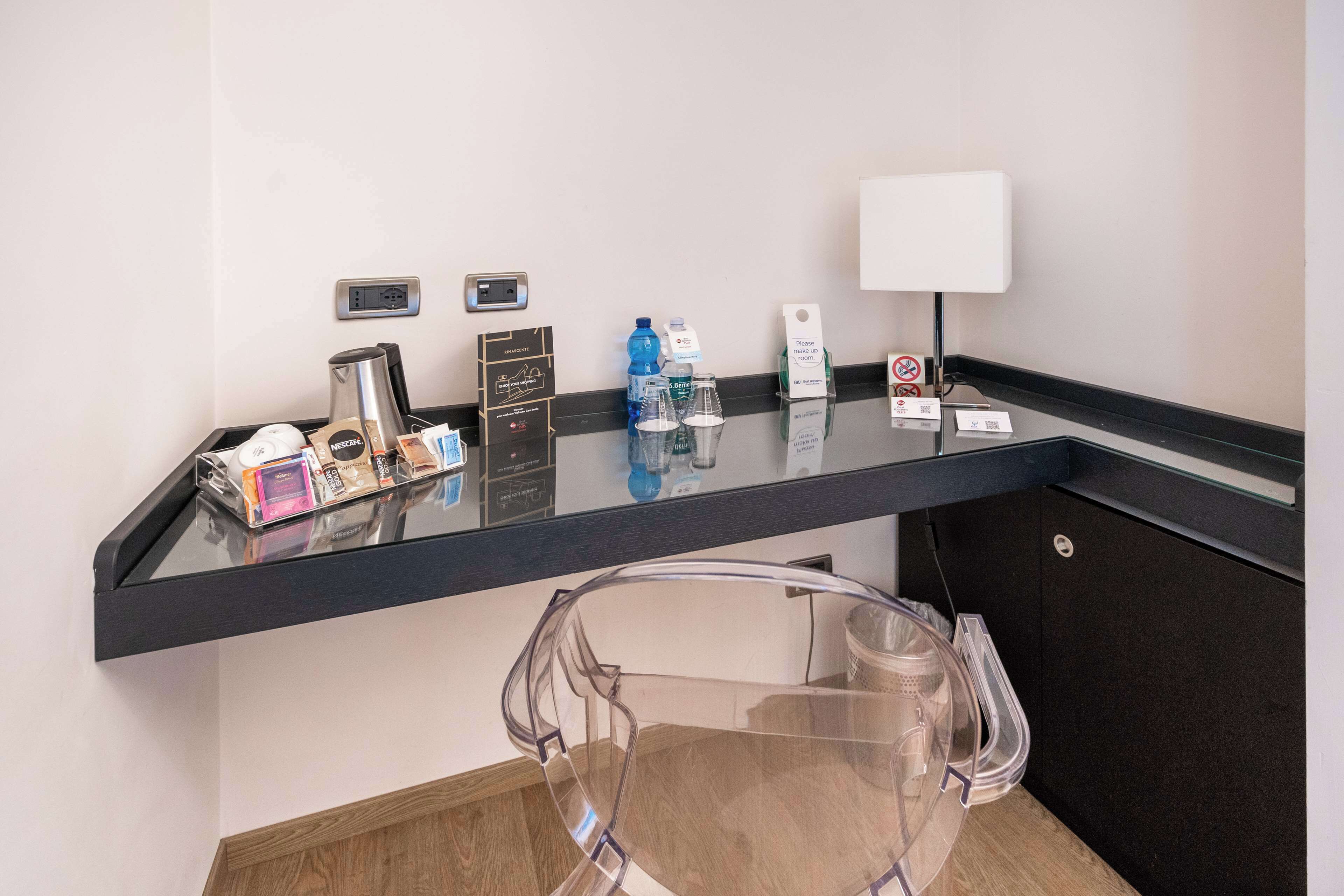 A hotel reception area with a glass counter, a coffee machine, a water dispenser, a trash bin, and a sign indicating no smoking.