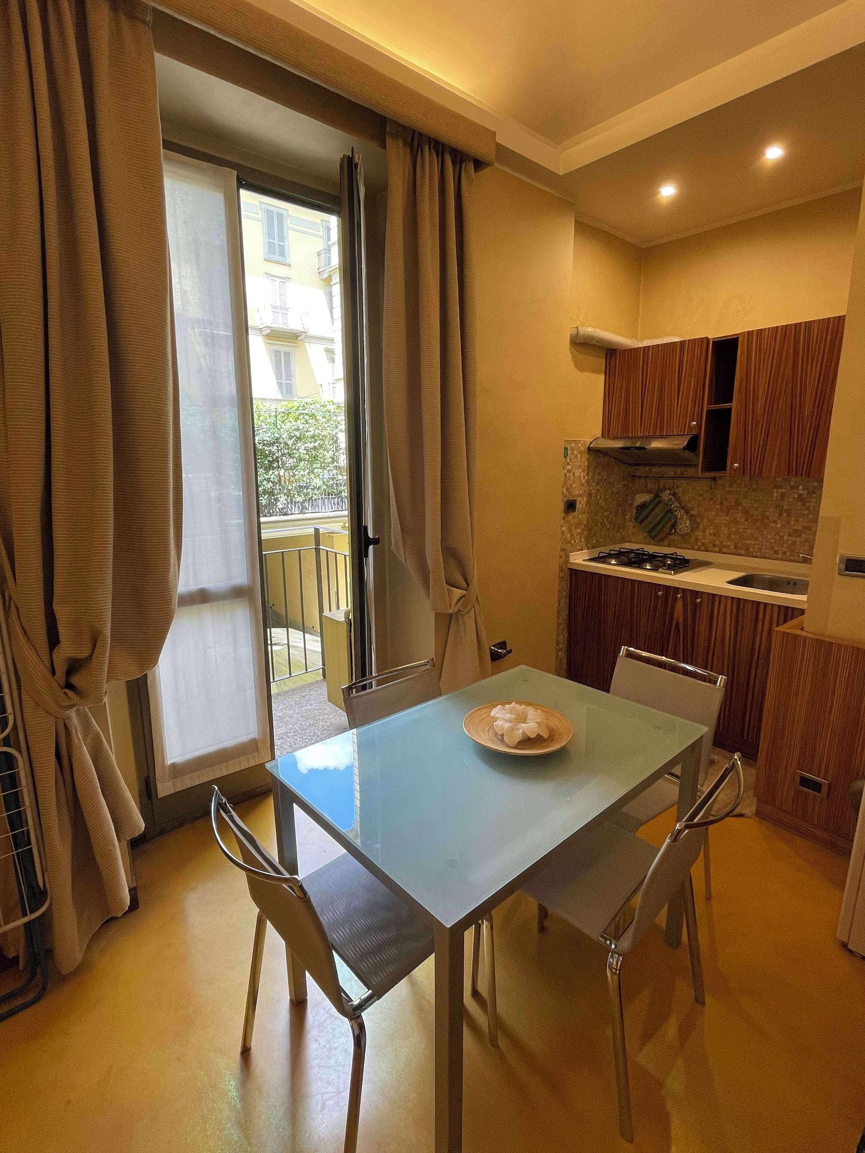 Une cuisine compacte avec un coin repas, une porte-fenêtre coulissante donnant sur un balcon et des meubles de rangement en bois.