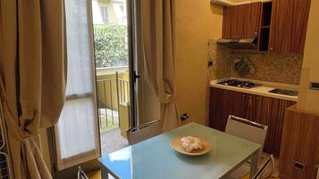 Une cuisine compacte avec un coin repas, une porte-fenêtre coulissante donnant sur un balcon et des meubles de rangement en bois.