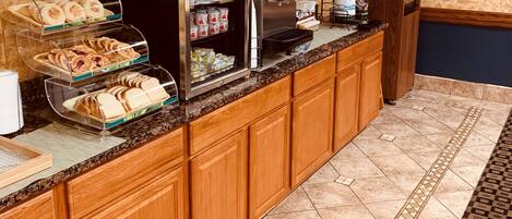 A breakfast bar with a coffee machine, a refrigerator, and a display case with pastries.