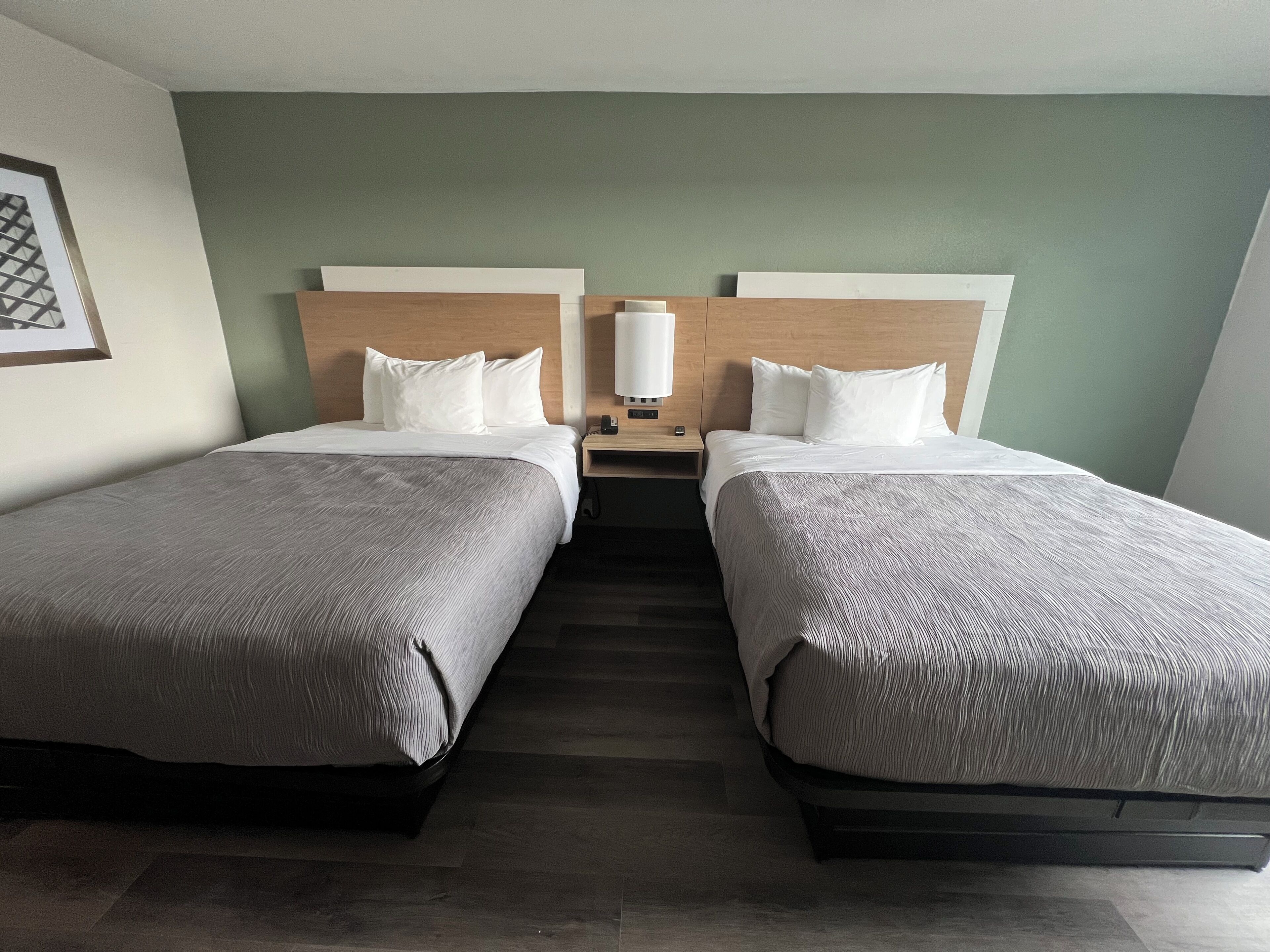 Une chambre d’hôtel avec deux lits, une table de chevet, une lampe et un tableau encadré au mur.