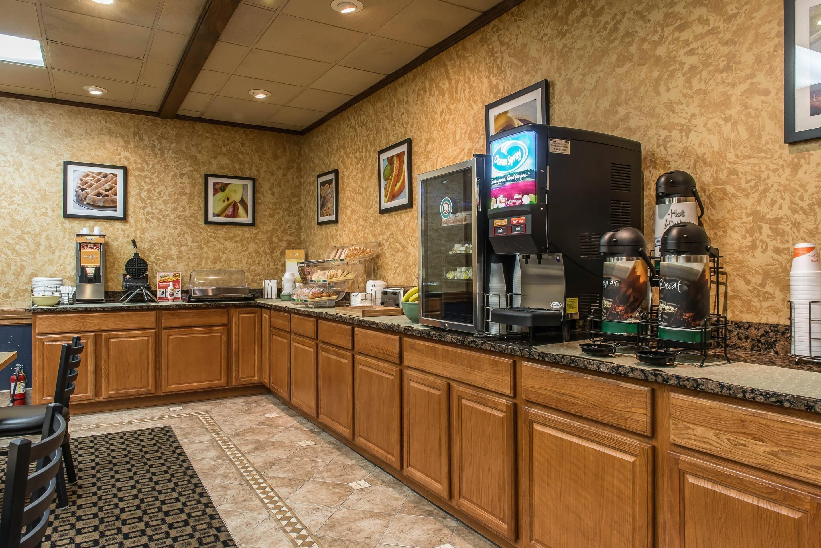 A hotel kitchen with wooden cabinets, a coffee machine, and a waffle maker.
