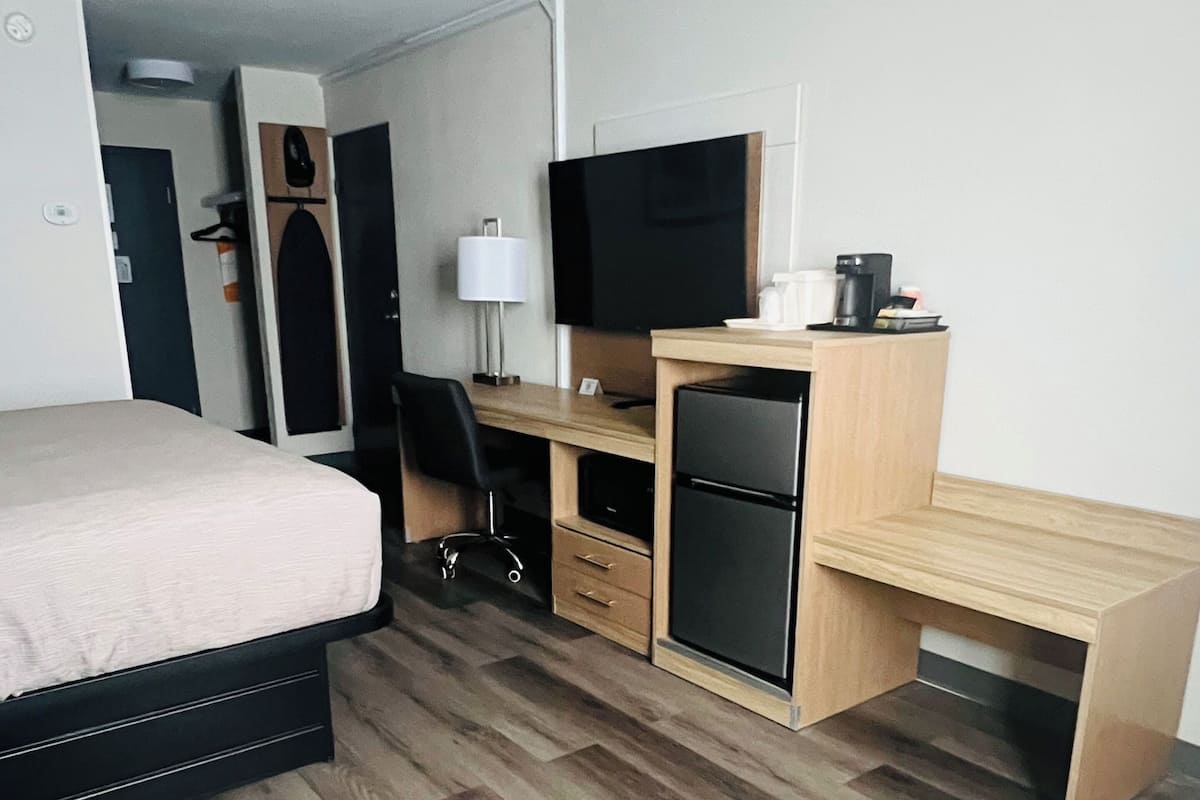 A hotel room with a bed, a desk, a television, and a refrigerator.